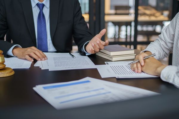 A lawyer in a suit gestures while discussing legal documents with a client at a conference table