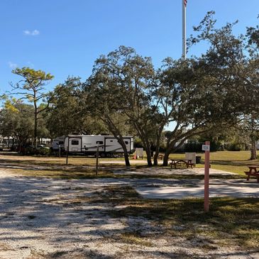 RV parked at a sunny campsite with picnic tables and tall trees.