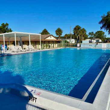 A clean outdoor swimming pool with chairs and umbrellas under a clear blue sky.
