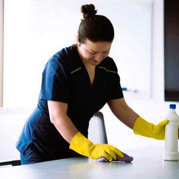 A woman in blue scrubs cleaning a surface with yellow gloves.