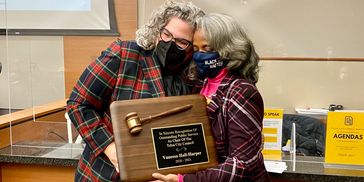 Two women sharing a warm moment while holding a recognition plaque.