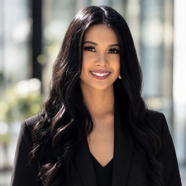 Confident woman with long black hair in a black blazer smiling outdoors.