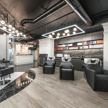 Modern hair salon with sleek black chairs and bright lighting.