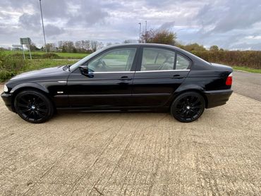Black BMW sedan with black rims parked on a gravel surface.
