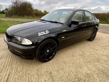 Black BMW sedan parked outdoors with a price tag of £1299 on the front side.