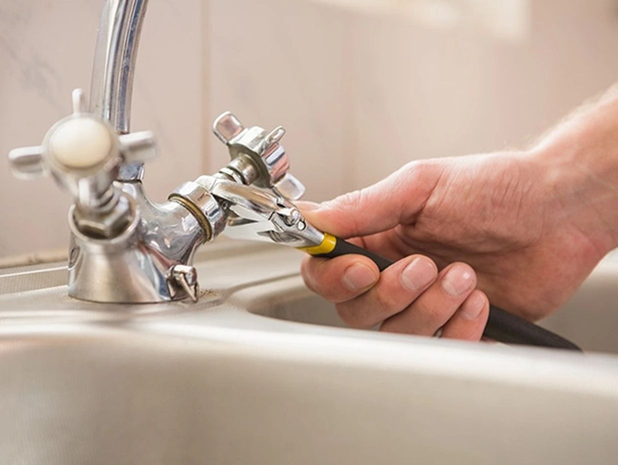 Hand using pliers to fix a kitchen faucet connection.