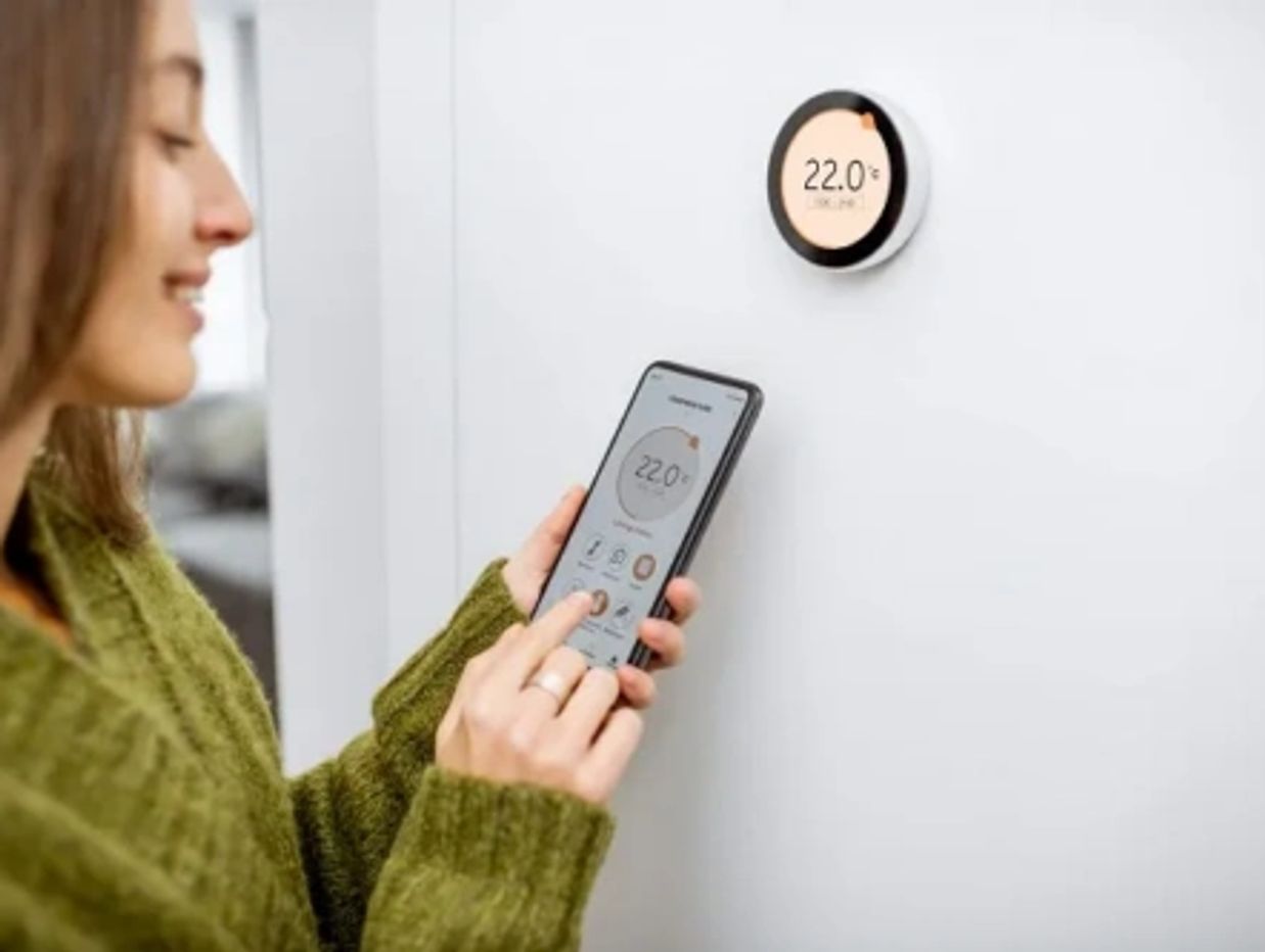 Woman adjusting smart thermostat temperature using smartphone app.