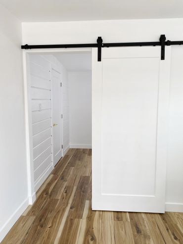 Modern white sliding barn door with black hardware in a room with wood flooring.
