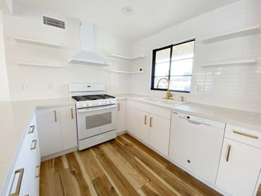 Bright modern kitchen with white cabinets, gold handles, and wooden flooring.
