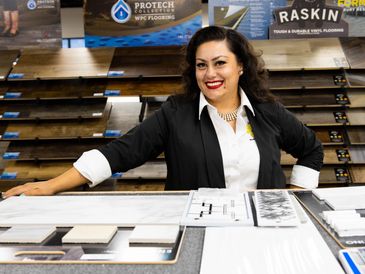 Smiling woman presenting flooring and tile samples in a showroom.