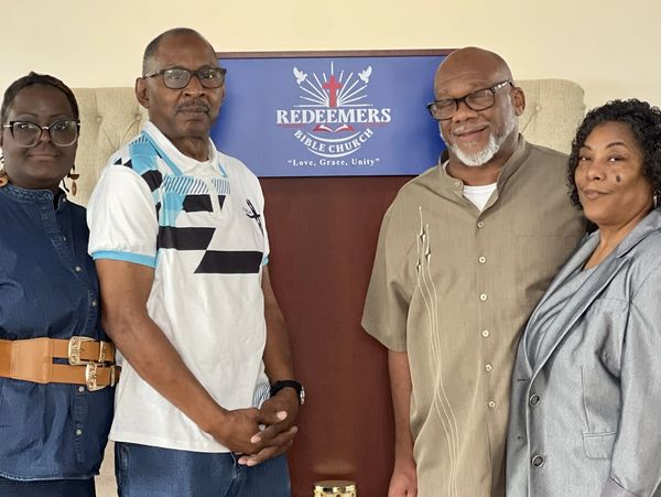 Four adults stand in front of a Redeemers Bible Church banner.