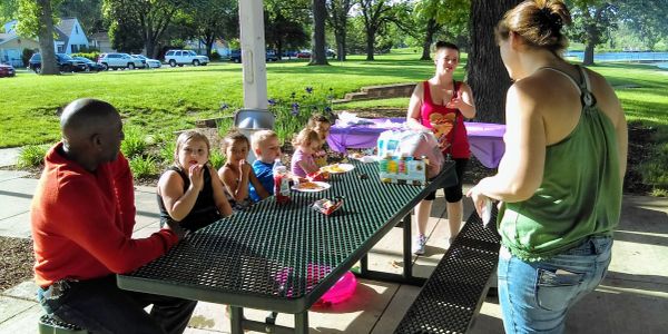 Children and adults enjoying a picnic at a park table on a sunny day.