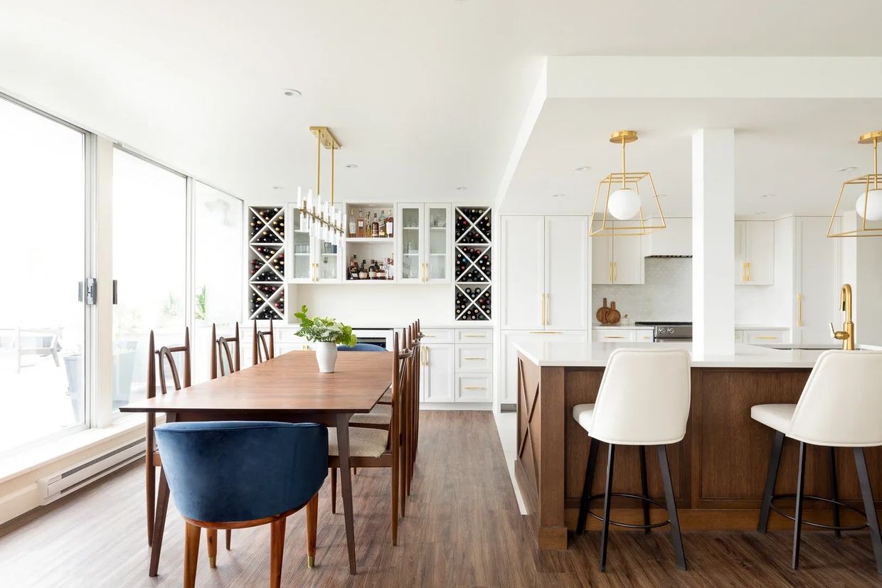 Modern kitchen and dining area with wood and white decor, gold accents, and large windows.