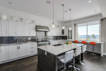 Modern kitchen with white cabinets, large island, and orange bar stools.