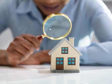 Person inspecting a miniature house with a magnifying glass.
