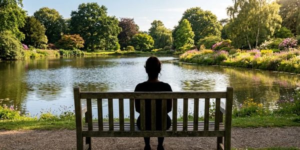 Person sitting alone on a bench by a peaceful lake in a park.
