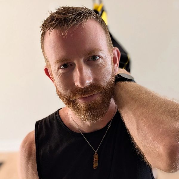 Man with red beard and black sleeveless shirt looking at camera.