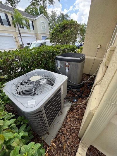 Two outdoor air conditioning units installed beside a building with greenery around.
