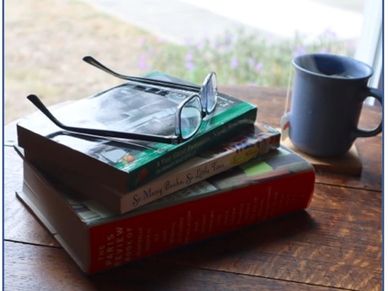 Stack of books with reading glasses and a coffee mug on a wooden table.