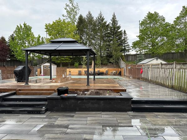 Backyard with gazebo, pool, and wet tiled patio after rain.