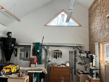 Woodshop with triangular window, bandsaws, dust collector, drill press, and thickness planer.