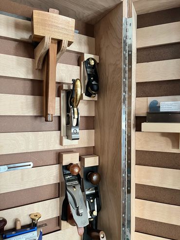 Hand planes and mallets hanging in cabinet lined with French cleats.