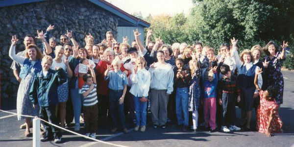 Large group of people posing outdoors, making hand signs together.