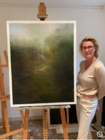 Artist standing beside an easel with an abstract painting in a studio.