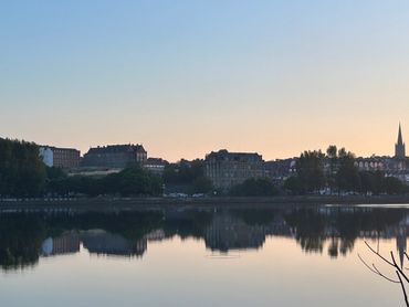 Tranquil cityscape reflected on calm river at sunset.