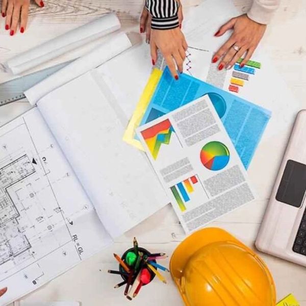 Hands examining construction plans and charts on a desk.