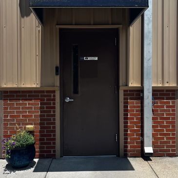 Closed dark brown door with brick wall and potted plant.