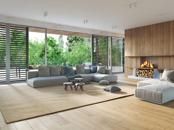 A modern living room with a gray sectional sofa, a light brown rug, a fireplace, and large windows.