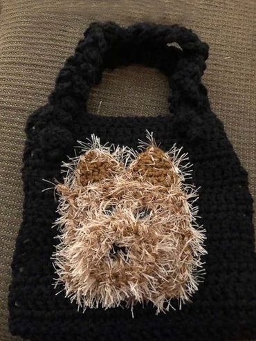 A bag made from yarn with a brown dog's face on the front.