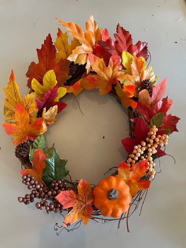 A fall wreath featuring leaves, a pumpkin and other fall elements.