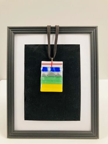 A ceramic pendant featuring green, blue, yellow, red and greay designs.