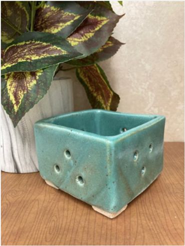 A short, square ceramic vase with holes on each side.