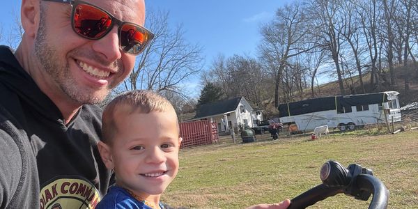 Man and child smiling outdoors on a sunny day.