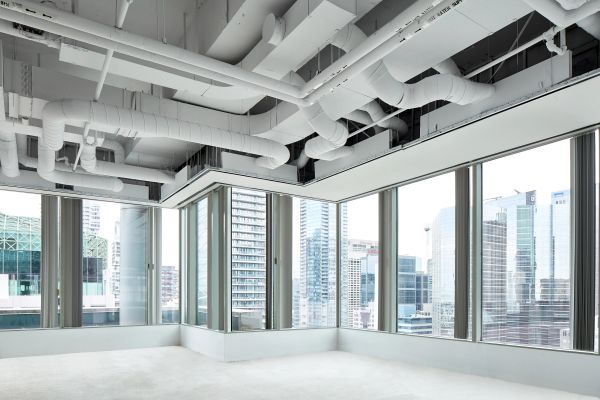 Empty office space with large windows and exposed ceiling pipes.