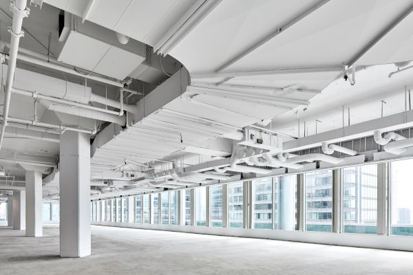 Large empty office space with exposed ceiling ducts and windows.