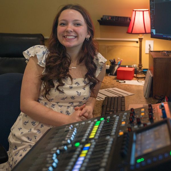 Young woman smiling at a sound mixing console in a cozy room.