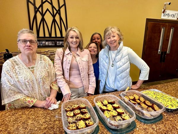 Five women smiling behind a table with homemade baked goods.