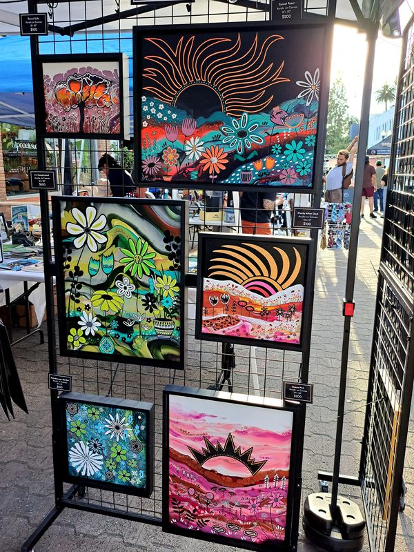 Colorful floral paintings displayed at an outdoor art market booth.