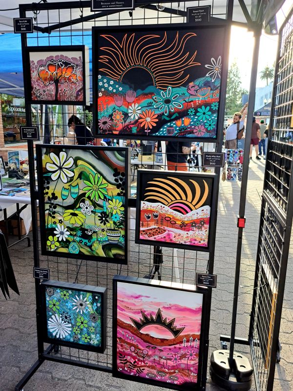 Colorful floral paintings displayed at an outdoor art market booth.