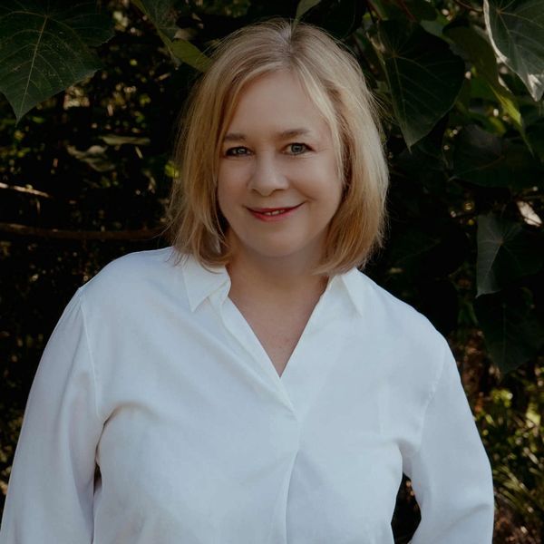 Smiling woman with blonde hair in a white shirt outdoors.