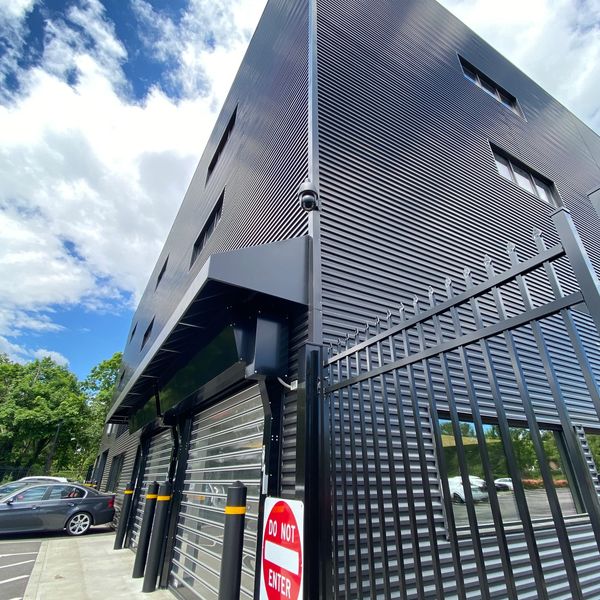 Modern black industrial building with security gate and 'Do Not Enter' sign.