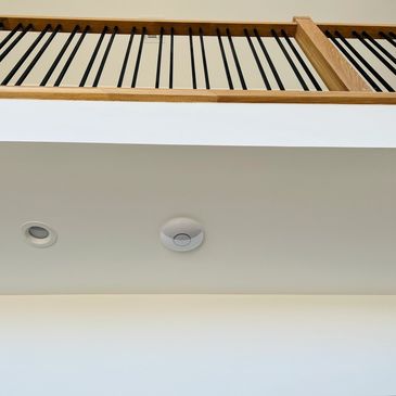 Ceiling with light fixture, smoke detector, and wooden railing above.