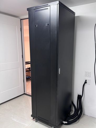 Tall black server rack cabinet on wheels in a clean room corner.