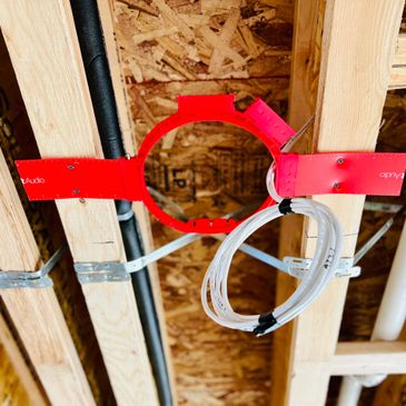 Red circular speaker mount attached to ceiling joists with white cables coiled inside.