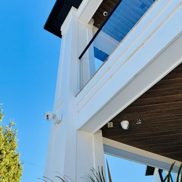 Modern white building corner with security cameras under clear blue sky.