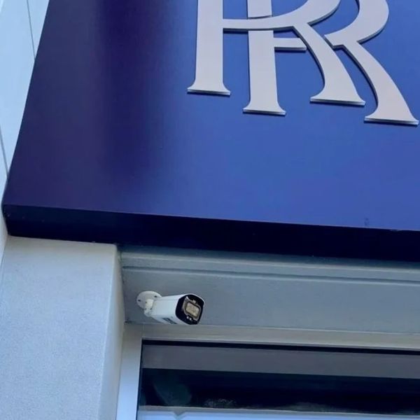 Rolls-Royce logo on a blue sign above a security camera at a building entrance.